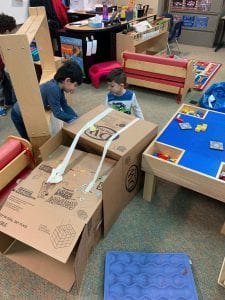 Two boys use boxes and tape and horizontally arrange the boxes to make an alligator trap.
