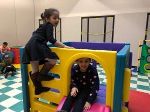 Indoor recess, two girls climbing on playground equipment.
