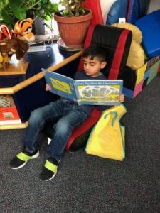 A preschool boy enjoys reading the pictures of his book while sitting in a cozy chair.