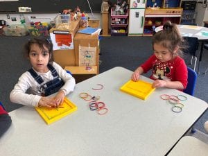 Two preschool girls make shapes on the geoboards with rubber bands.
