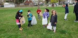Preschoolers have plastic bags and are cleaning trash up in their playground.