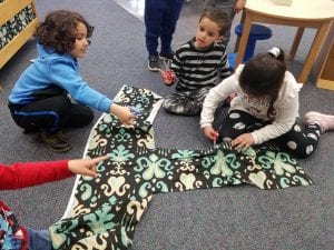 Preschoolers work together to cut material for class cushions.