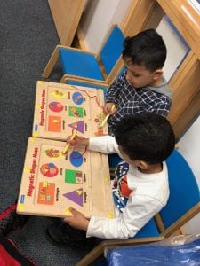 Two boys sit next to each other working on wooden boards with magnetic shapes.