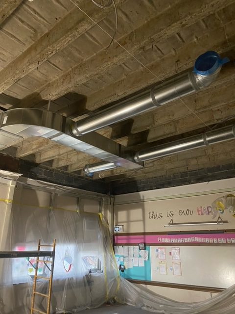 HVAC ducts are being installed in an exposed ceiling at Whitmore Bolles Elementary School.
