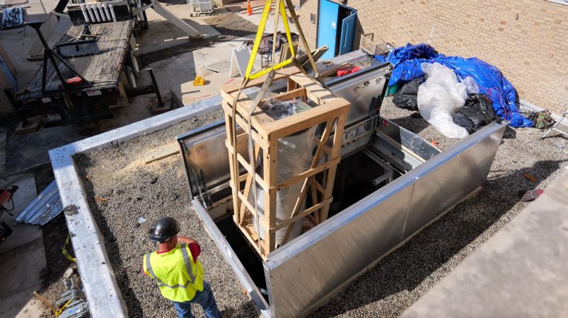 Crews use a crane to lift new HVAC equipment through a new roof hatch into Whitmore Bolles Elementary School in August 2023.