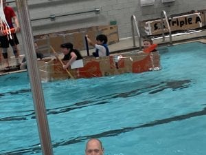 Kids rowing cardboard boat.