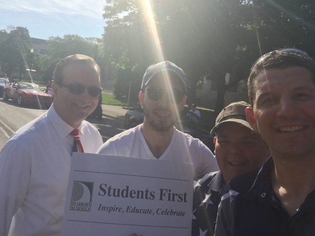 Adults with the student first sign at the memorial day parade. 