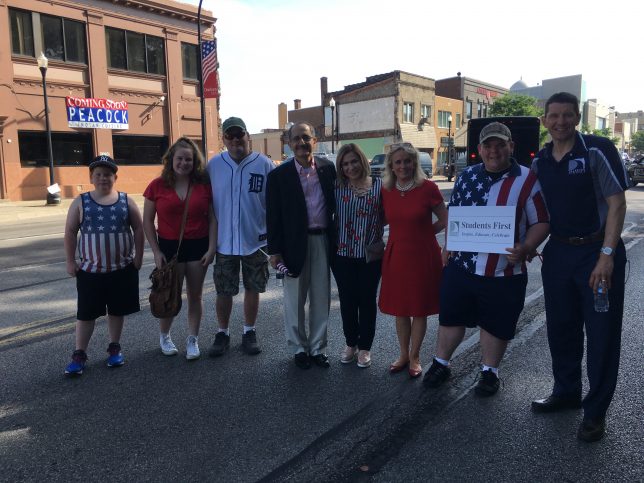 Adults with the student first sign at the memorial day parade. 