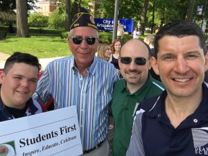 Adults with the student first sign at the memorial day parade. Selfie version