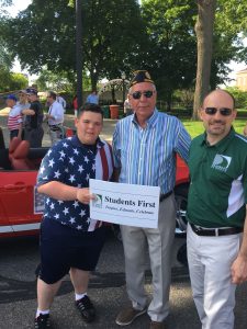 Adults with the student first sign at the memorial day parade. Judge and Trustee