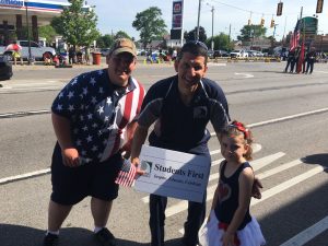 Students first sign and 2 adults and a student at the parade. 