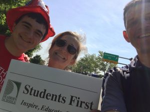 2 adults, and student the sign and a selfie at the parade