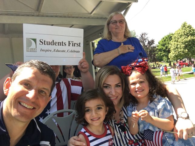 Several individuals with the vision sign watching the parade. Trustee Hammoud and her two children. 