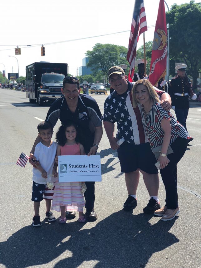 3 adults and two cute children with the sign at the parade. 