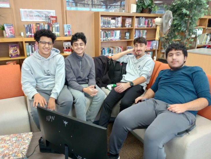 Four students sit on a school library couch playing a video game.