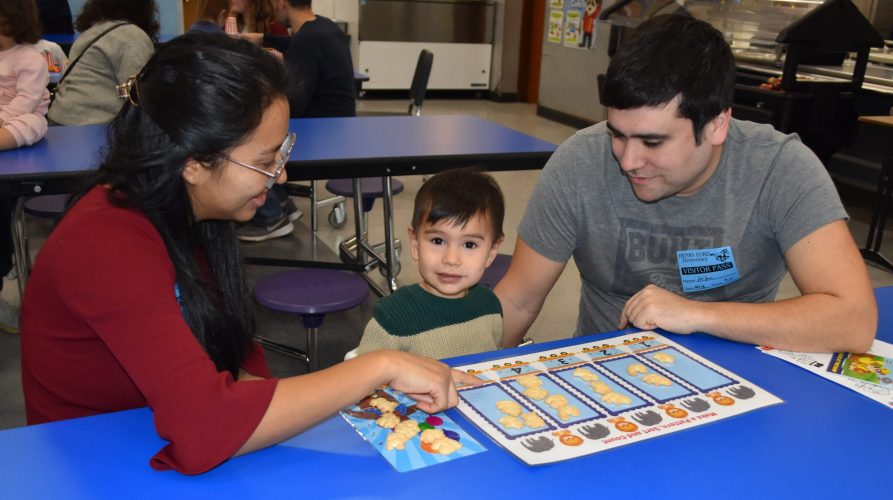 Two adults help a young child count crackers on a counting sheet.