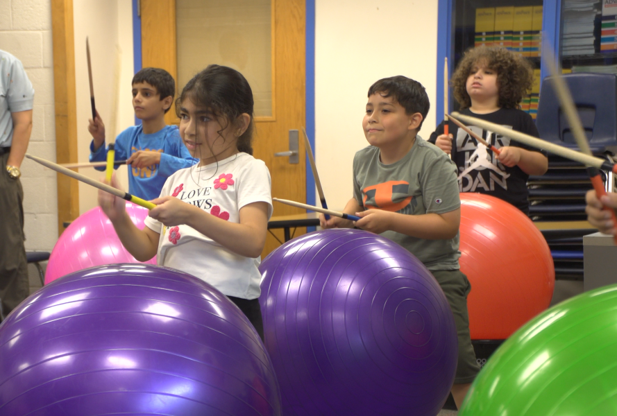 Students participate in cardio drumming, using drumsticks on large yoga balls.