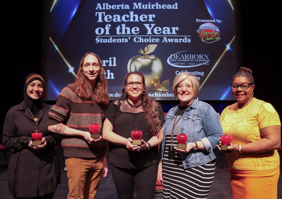 Five people stand on stage holding glass apple awards.