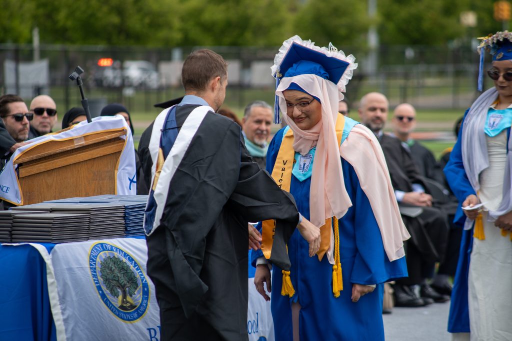 A student in a blue cap and gown receives special honors during graduation