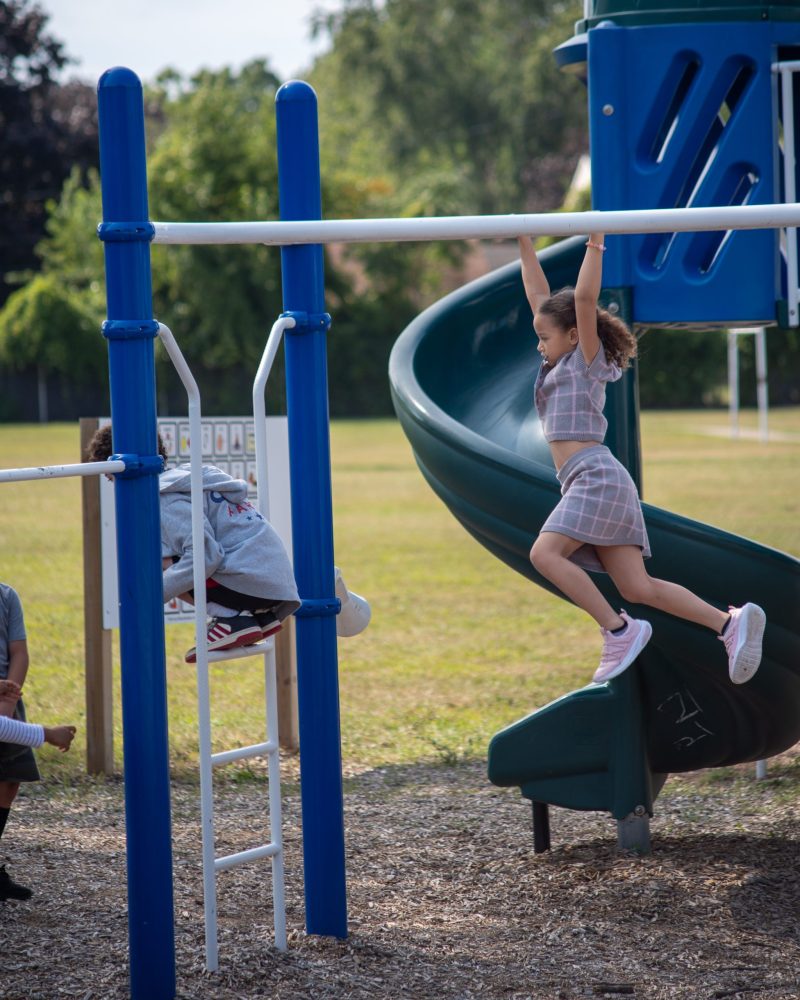A student climbs across a play structure at Nowlin