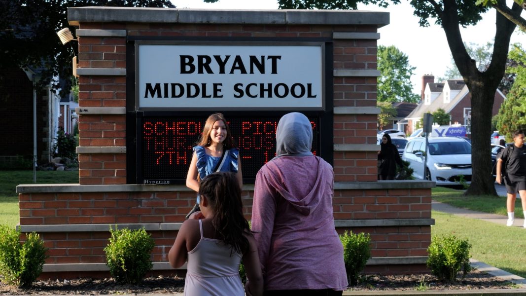 A girl poses for a photo by her mother in front of the Bryant Middle School sign on the first day of school.
