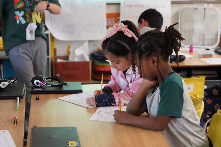 Two young students work on papers at their desk